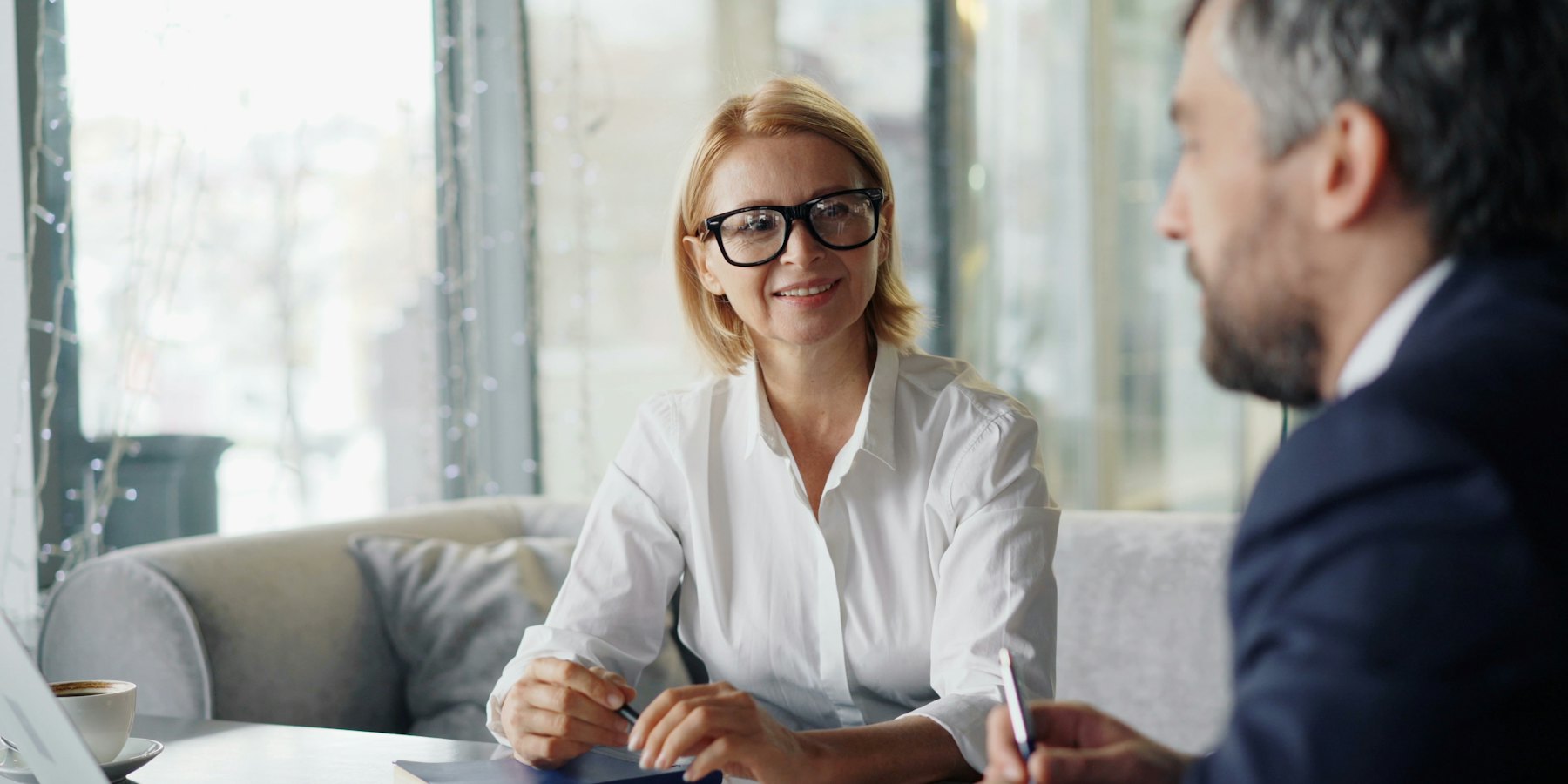 Corretora sorrindo durante atendimento a um cliente, com notebook na mesa