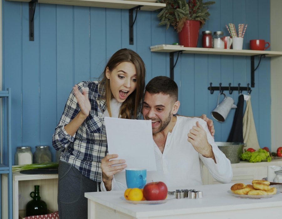Casal comemorando ao ler um documento na cozinha