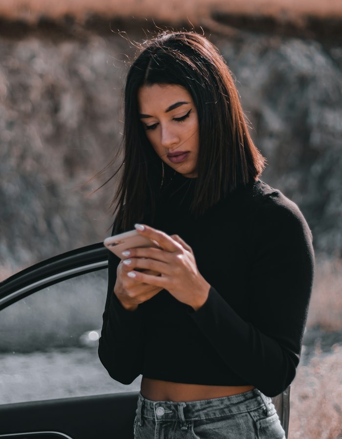 Mulher ao lado do carro olhando o celular